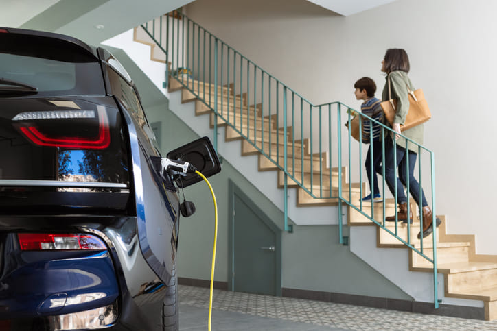 maman et son enfant montent escalier garage avec voiture electrique branchee